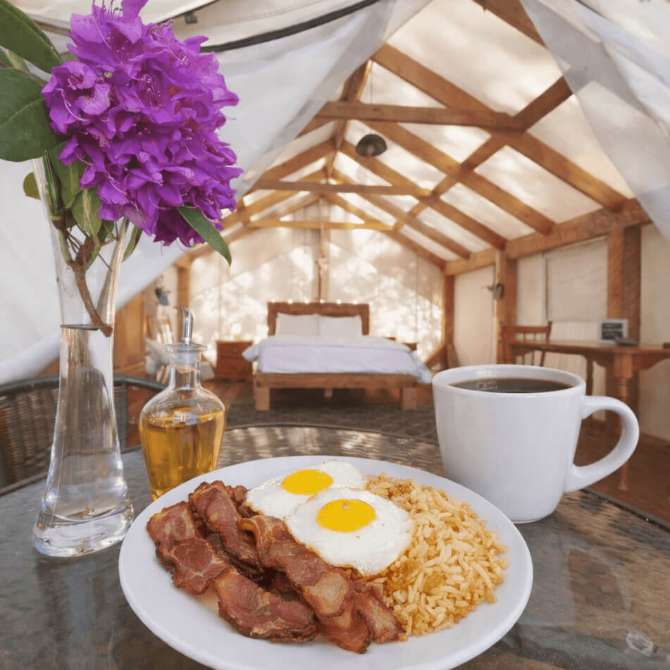 Prepared breakfast plate on an outdoor table with flowers, with the inside of a glamping tent in the background