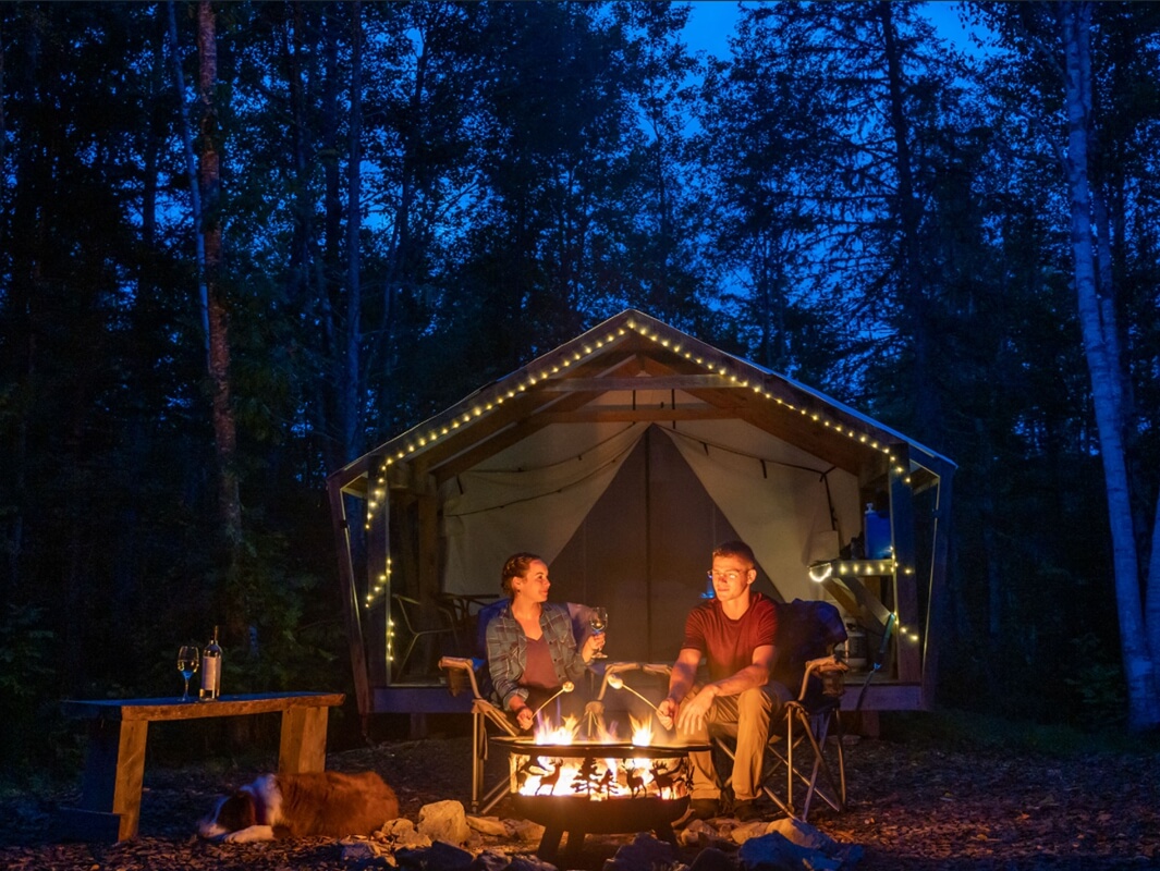 Couple enjoying a campfire outside a glamping tent at night in Nova Scotia forest