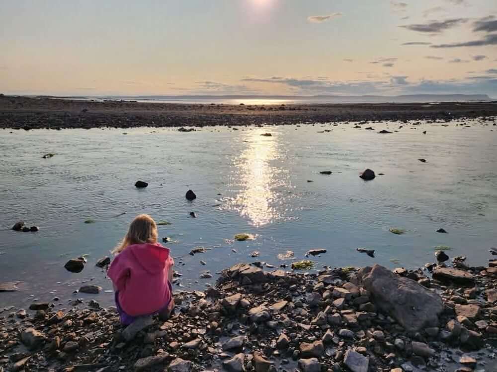 Person sitting on the rocky shoreline of the Minas Basin at sunset in Nova Scotia
