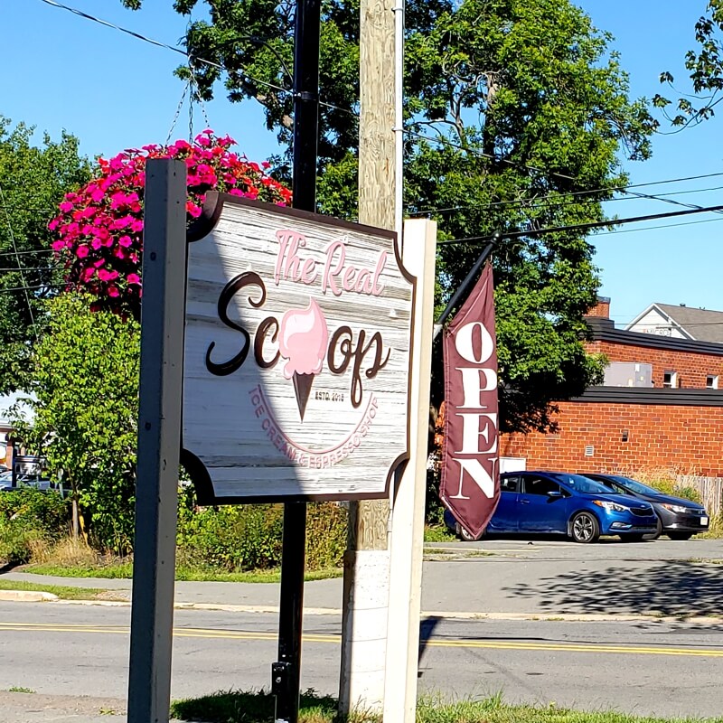 The Real Scoop ice cream shop sign in Wolfville, Nova Scotia, with flowers and open flag