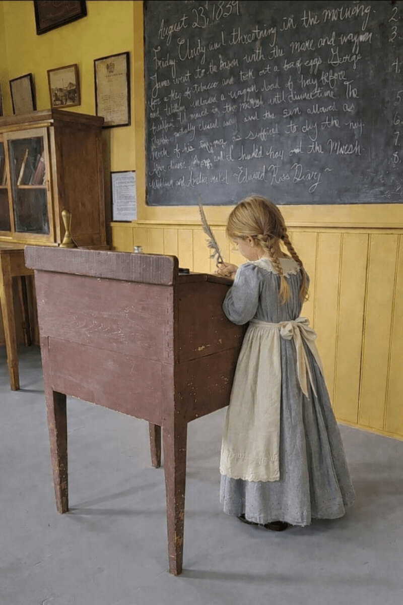 Child writing with quill in historic schoolhouse at Ross Farm Museum New Ross Nova Scotia living history experience